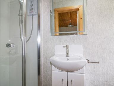 A bathroom with a shower enclosure a sink with cabinet and a mirror reflecting a wooden ceiling at Lodge One in Brighton near Summercourt