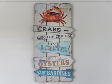 A wall sign with a crab and arrows pointing to different seafood options including crabs live lobster oysters and fresh sardines at Thimble Cottage in Mevagissey
