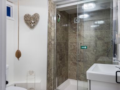 A bathroom with a tiled shower enclosure a white sink and a toilet with a heart-shaped wall decoration at Thimble Cottage in Mevagissey