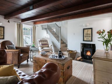 A living room with wooden beams a fireplace leather and fabric chairs a chest coffee table and a staircase at Thimble Cottage in Mevagissey