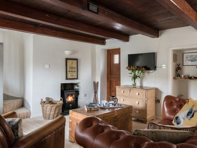 A living room with wooden beams leather chairs a wood stove and a wooden chest at Thimble Cottage in Mevagissey