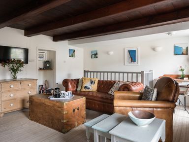 A living room with leather sofas wooden chest table and a dresser with flowers at Thimble Cottage in Mevagissey