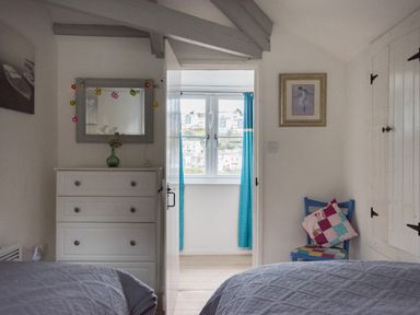 A bedroom with two beds facing a white dresser and a blue chair with cushions at Thimble Cottage in Mevagissey