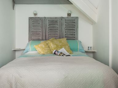 A bed with patterned pillows and a quilt in a room with sloped ceilings at Thimble Cottage in Mevagissey