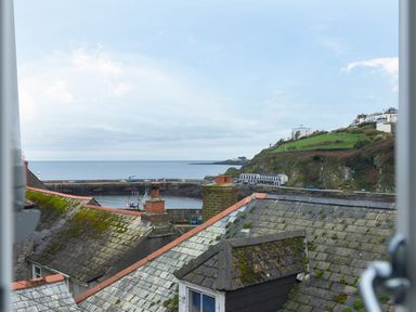 A view of rooftops with chimneys overlooking a harbor and green hillside at Thimble Cottage in Mevagissey