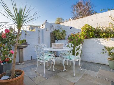 An outdoor patio with a white metal table and chairs surrounded by potted plants and flowers at Thimble Cottage in Mevagissey