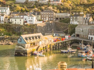 A harbor with boats docked near stone buildings and houses on a hillside at Thimble Cottage in Mevagissey