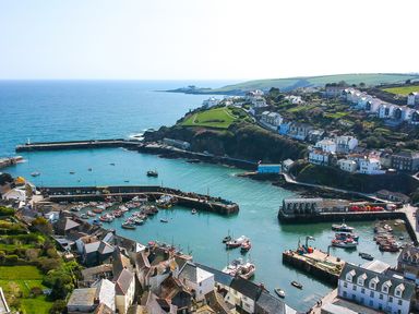 A coastal harbor with boats docked in the water surrounded by houses and green hills at Thimble Cottage in Mevagissey
