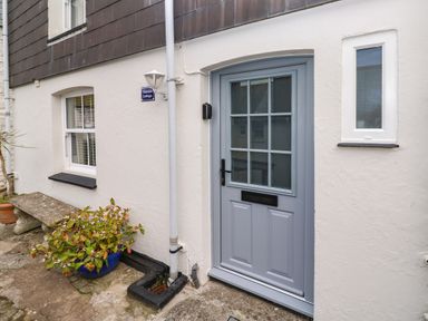 A blue front door next to a window with a concrete bench and a potted plant outside at Thimble Cottage in Mevagissey