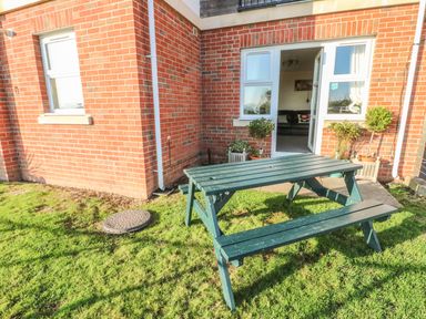 A green wooden picnic table on grass outside a brick building with a door and windows at Beach View in Benllech near Red Wharf Bay