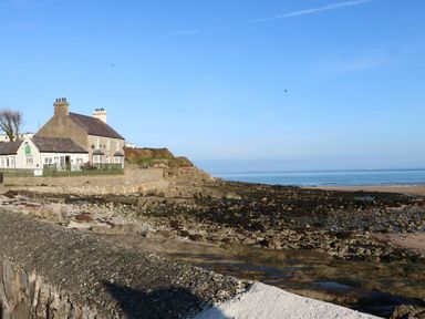 A house near a rocky beach with the sea and blue sky at Beach View in Benllech near Red Wharf Bay