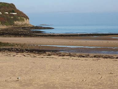 A sandy beach with rock formations and a cliffside with houses near calm sea at Beach View in Benllech near Red Wharf Bay