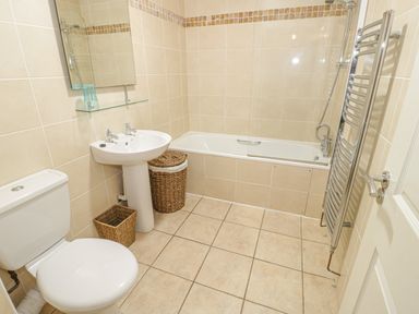 A bathroom with a toilet sink bathtub wall mirror towel rail and wicker baskets at Beach View in Benllech near Red Wharf Bay