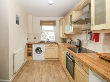 A kitchen with wooden cabinets and countertops a washing machine an oven a stove and a window at Beach View in Benllech near Red Wharf Bay