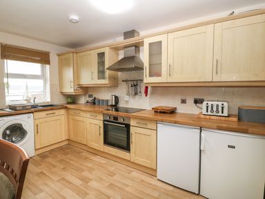 A kitchen with wooden cabinets a washing machine an oven a stovetop a toaster and a window at Beach View in Benllech near Red Wharf Bay