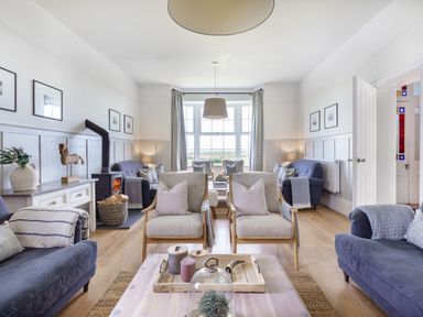 A living room with multiple armchairs sofas a wood stove and a large window at Ty Carmel in Rhosneigr
