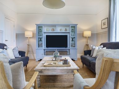 A living room with sofas a wooden coffee table a blue entertainment unit and two standing lamps at Ty Carmel in Rhosneigr