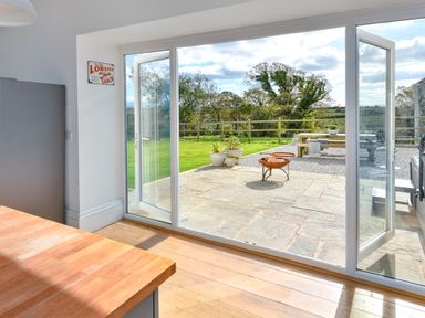A kitchen with wooden countertop and glass sliding doors opening to a patio with flower pots and fire pit at Ty Carmel in Rhosneigr
