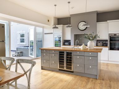 A kitchen with a large island and wooden top with vases and open doors leading outside at Ty Carmel in Rhosneigr