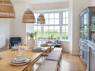 A dining room with wooden table set for six and large windows showing a green field at Ty Carmel in Rhosneigr