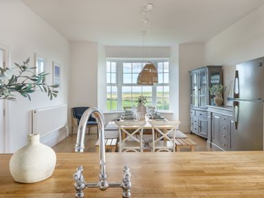 A dining area with a wooden table set for a meal with chairs and benches a cabinet and a refrigerator in the background at Ty Carmel in Rhosneigr