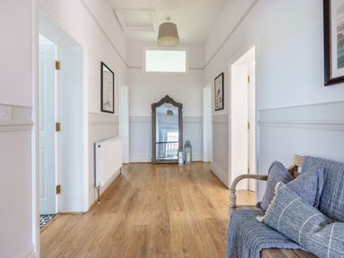 A hallway with wooden flooring a large mirror two lanterns a bench with cushions and framed pictures at Ty Carmel in Rhosneigr