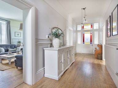 A hallway with a white sideboard and vase a wooden bench and stained glass front door at Ty Carmel in Rhosneigr