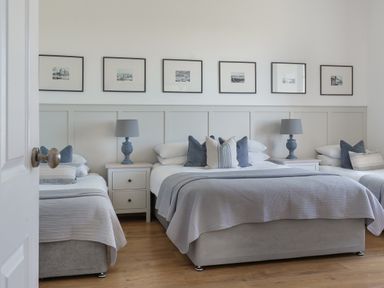 A bedroom with three beds two nightstands two lamps and six framed pictures on the wall at Ty Carmel in Rhosneigr