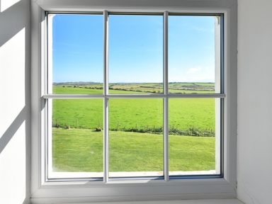 A window with white frame showing green fields and blue sky at Ty Carmel in Rhosneigr