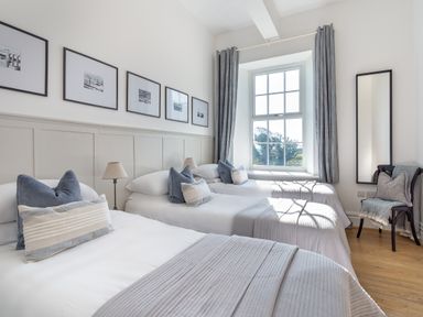 A bedroom with three single beds pillows lamps framed pictures a window with curtains a chair and a full length mirror at Ty Carmel in Rhosneigr