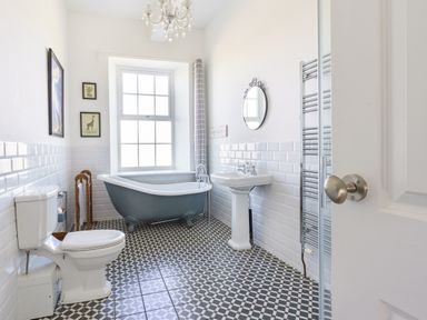 A bathroom with a toilet, clawfoot bathtub, pedestal sink, mirror, towel rack, and framed pictures at Ty Carmel in Rhosneigr