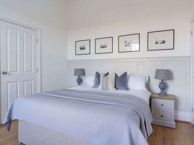 A bedroom with a bed with pillows and blankets lamps on bedside tables and framed pictures on the wall at Ty Carmel in Rhosneigr