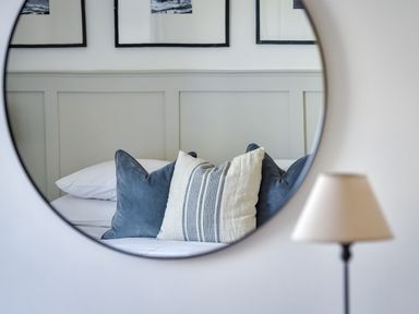 A reflection of a bed with pillows and a lamp in a round mirror at Ty Carmel in Rhosneigr