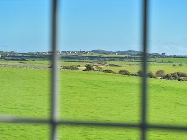 A green field with trees and distant houses seen through a window grid at Ty Carmel in Rhosneigr