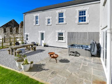 An outdoor patio area with a hot tub wooden picnic table fire pit and potted plants at Ty Carmel in Rhosneigr