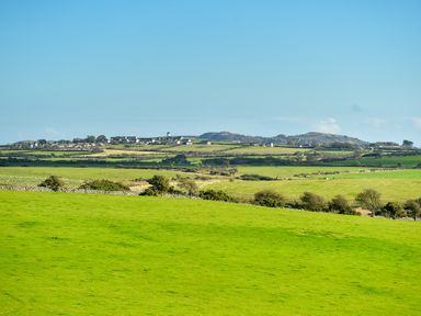 Green fields with scattered trees and houses in the background under a clear sky at Ty Carmel in Rhosneigr