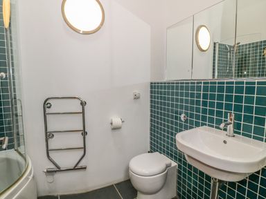 A bathroom with a toilet a sink a heated towel rail and teal tiled walls at Y Beudy in Criccieth