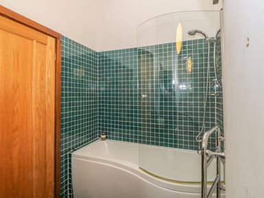 A bathroom with a bathtub shower and green tiled walls at Y Beudy in Criccieth