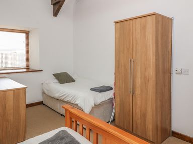 A bedroom with two single beds a wooden wardrobe a wooden chest of drawers and a window with blinds at Y Beudy in Criccieth