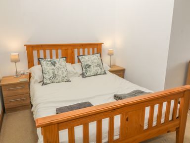 A bedroom with a wooden bed with white bedding two floral pillows and bedside tables with lamps at Y Beudy in Criccieth