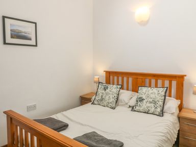 A bedroom with a wooden bed with patterned pillows two bedside tables with lamps and a framed picture on the wall at Y Beudy in Criccieth