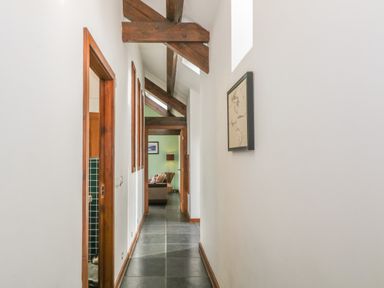 A hallway with dark tiled floor wooden beams and framed artwork leading to a room with a sofa at Y Beudy in Criccieth