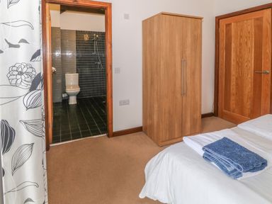 A bedroom with a bed showing folded towels a wooden wardrobe a wooden door and an open doorway to a bathroom at Y Beudy in Criccieth