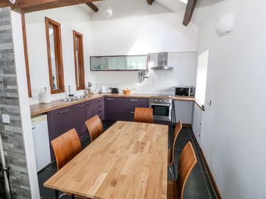 A kitchen with a wooden dining table and chairs and purple cabinets at Y Beudy in Criccieth