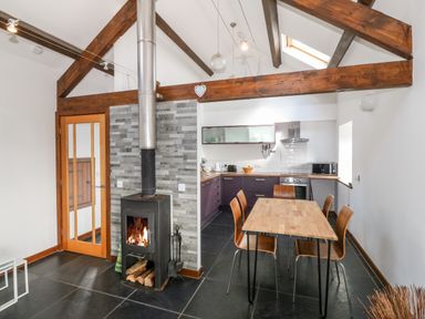 A kitchen and dining area with wood burning stove and exposed wooden beams at Y Beudy in Criccieth