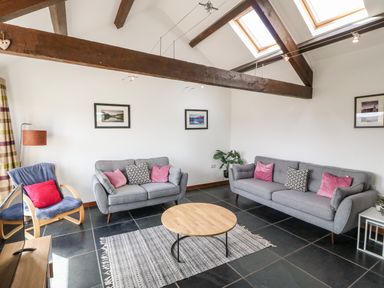 A living room with grey sofas pink and black cushions wooden beams and skylights at Y Beudy in Criccieth