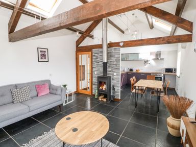 An open plan living room and kitchen with a fireplace and wooden beams at Y Beudy in Criccieth