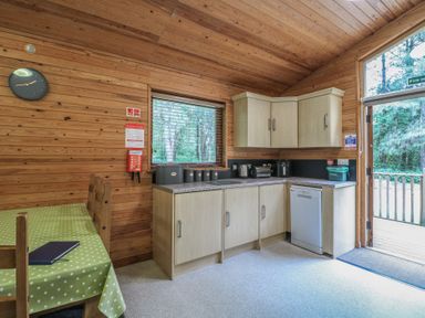 A kitchen with wooden walls, cabinets, countertop appliances, a table with chairs, and a door leading outside at Birch Lodge in Rosliston