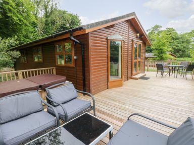 An outdoor wooden deck with seating area and hot tub next to a wood cabin at The Beeches in Narberth