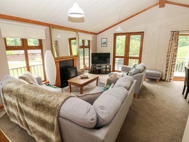 A living room with two grey sofas a wooden coffee table a television and large windows at The Beeches in Narberth